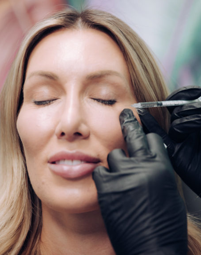 A woman receiving a cosmetic injection near her eye, administered by a professional wearing black gloves.