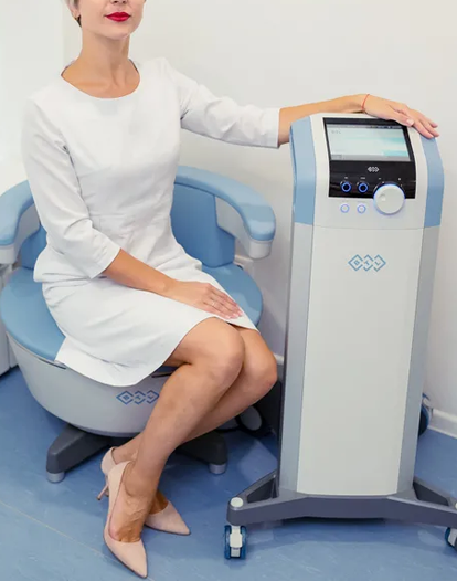 A woman in a white dress seated on a wellness treatment chair next to a modern medical device.