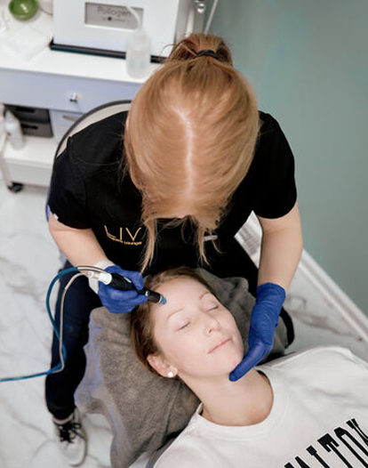 A technician performing a facial treatment on a client lying down, using advanced skincare equipment