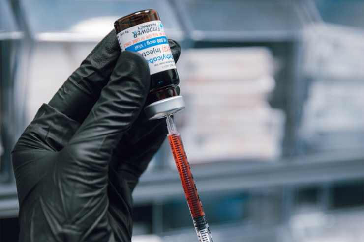 A gloved hand holding a vial of medication and a syringe with a needle.